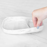 A hand holds a Bumkins Silicone Grip Tray: Marble, demonstrating the suction cup bottom on a marble surface.