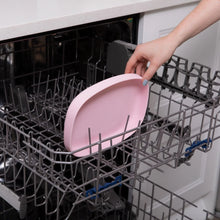 Load image into Gallery viewer, A hand places a Bumkins Silicone Grip Tray: Pink into the top rack of an open dishwasher.