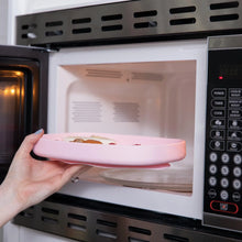 Load image into Gallery viewer, A hand places a Bumkins Silicone Grip Tray: Pink filled with food into an open microwave.
