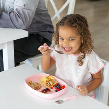 Load image into Gallery viewer, A girl with curly hair enjoys breakfast from a Bumkins Silicone Grip Tray: Pink filled with eggs, berries, and toast at a white table.