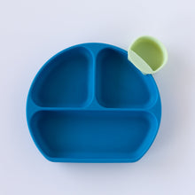 Load image into Gallery viewer, A light green dipping cup rests on the edge of Bumkins Silicone Grip Dish: Dark Blue on a white background.