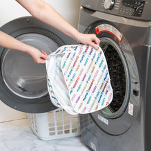 Load image into Gallery viewer, A person holds a Bumkins Packing Cube 2 Pack: Mickey & Friends Varsity in front of an open front-loading washing machine.