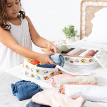 Load image into Gallery viewer, A girl in a white dress uses the Bumkins Packing Cube 2 Pack: Winnie + Friends to organize clothes on a bed.