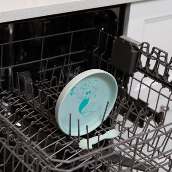 Bumkins Silicone Plate + Spoon Set: Disney Princess Ariel sits in the top rack of an open dishwasher.