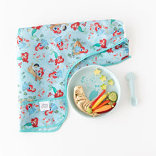 Load image into Gallery viewer, Bumkins Silicone Plate + Spoon Set: Disney Princess Ariel, holding hummus, carrots, and cucumber, sits beside a bib on a white background.