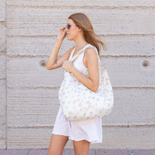 Load image into Gallery viewer, A woman in a white dress and sunglasses walks by a textured wall, carrying Bumkins Packable Tote Bag: Palm Daze.