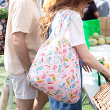 Load image into Gallery viewer, A person with a Bumkins Packable Tote Bag: Boots browses fresh fruits at an outdoor market.