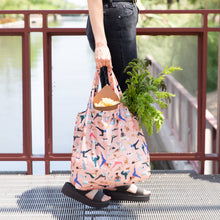Load image into Gallery viewer, A person holding a Bumkins Packable Tote Bag: Yoga Pals with groceries, including greens, stands on a metal bridge.
