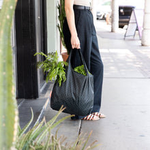 Load image into Gallery viewer, A person on a sidewalk holding a Bumkins Packable Tote Bag: Rich Black filled with fresh green leafy veggies.