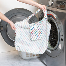 Load image into Gallery viewer, Someone holds a Bumkins Packable Tote Bag: Mickey & Friends Varsity in front of an open washing machine.