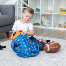 Load image into Gallery viewer, A child packs a soccer ball into a blue Bumkins Packable Tote Bag: Mickey & Friends Forever, with a football nearby on the rug.