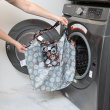 Load image into Gallery viewer, A person holds a Bumkins Packable Tote Bag: Ghostly Gallery in front of an open front-loading washing machine.