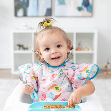 Load image into Gallery viewer, A toddler sits in a high chair, wearing a Bumkins Ruffle Apron Bib: Boots and holding a fork and spoon over a blue plate of waffles.