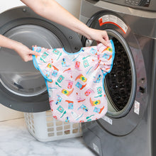 Load image into Gallery viewer, A person holds Bumkins Ruffle Apron Bib: Boots in front of an open front-loading washing machine.