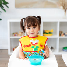 Load image into Gallery viewer, A girl in pigtails wearing a Bumkins SuperBib® 2 Pack: Super Mario™ Expressions smiles in a high chair with a blue bowl on the tray.