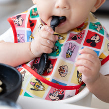 Load image into Gallery viewer, A child in a bright Bumkins SuperBib® 3 Pack: Mickey & Friends MVP holds a spoon, ready to eat from a bowl.