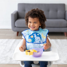 Load image into Gallery viewer, A curly-haired child smiles in a high chair, wearing a Bumkins SuperBib® 3 Pack: Stitch Star-ring Up Trouble and eating from a purple bowl.