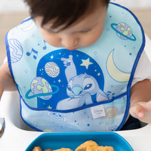 Load image into Gallery viewer, A child, sitting in a high chair, wears Bumkins SuperBib® 3 Pack: Stitch Star-ring Up Trouble and looks down at food on a blue plate.