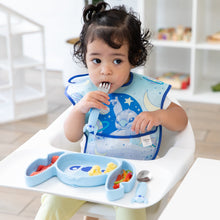 Load image into Gallery viewer, A girl wearing a Bumkins SuperBib® 3 Pack: Stitch Star-ring Up Trouble eats from a matching plate in a high chair in a bright playroom.