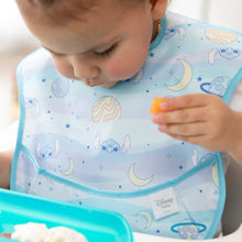 Load image into Gallery viewer, A toddler in a Bumkins SuperBib® 3 Pack: Stitch Star-ring Up Trouble holds orange food while looking down at a blue tray.