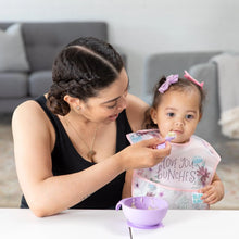 Load image into Gallery viewer, A woman in a black tank top feeds a toddler wearing a Bumkins SuperBib® 3 Pack: Love You Bunches from a purple bowl at a white table.