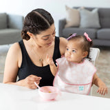 A woman and toddler wearing a Bumkins SuperBib® 3 Pack: Love You Bunches sit at a white table with a pink bowl & spoon.