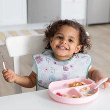 Load image into Gallery viewer, A curly-haired toddler sits at a table, wearing a Bumkins SuperBib® 3 Pack: Love You Bunches and eating from a pink plate with pink utensils.