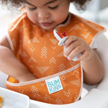 Load image into Gallery viewer, A toddler uses a spoon to eat berries while wearing an orange Bumkins SuperBib® 3 Pack: Desert Boho. Their hand reaches into the pocket.