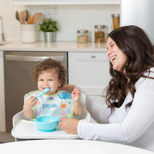 Load image into Gallery viewer, A smiling woman sits by a toddler in a high chair wearing a Bumkins SuperBib® 3 Pack: Rolling With the Waves eating from a blue bowl.