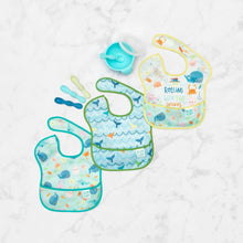 Load image into Gallery viewer, Bumkins SuperBib® 3 Pack: Rolling With the Waves lays flat on a marble surface with a blue bowl & spoon set and 3 toddler spoons nearby.