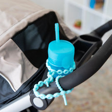 Load image into Gallery viewer, A blue cup with a straw in the cup holder of a stroller is secured to the handle with a Bumkins Silicone Accessory Tether 2-Pack: Blue.