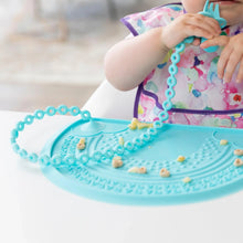 Load image into Gallery viewer, A child in a bib chews a silicone fork attached to a blue placemat with a Bumkins Silicone Accessory Tether 2-Pack: Blue.