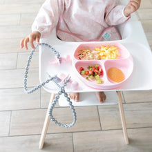 Load image into Gallery viewer, A baby in a high chair enjoys food from a plate, with toddler utensils secured to the tray by Bumkins Silicone Accessory Tether 2-Pack: Gray.