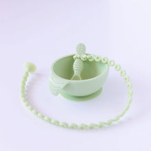 Load image into Gallery viewer, A Bumkins Silicone Accessory Tether 2-Pack: Sage is attached to a green spoon in a green bowl on a white background.