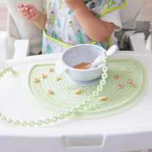 Load image into Gallery viewer, A child in a high chair enjoys a meal from a bowl on a placemat, with a spoon secured by a Bumkins Silicone Accessory Tether 2-Pack: Sage.