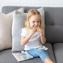 Load image into Gallery viewer, A blonde girl in a white shirt and jeans eats cookies from Bumkins Reusable Snack Bag, 3-Pack: Princess Magic, Ariel, and Jasmine on her lap.