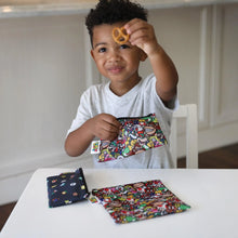 Load image into Gallery viewer, A child holds a pretzel at a white table with Bumkins Reusable Snack Bag, 3-Pack: Super Mario™ Power Up.