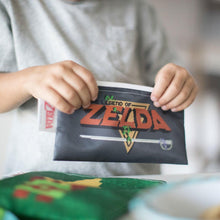 Load image into Gallery viewer, Close-up of a child in a gray shirt holding a Bumkins Reusable Snack Bag, 3-Pack: The Legend of Zelda™.