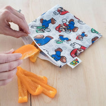 Load image into Gallery viewer, Hands place orange pepper slices into a Bumkins Reusable Snack Bag, Large: Super Mario™ & Luigi on a wooden surface.