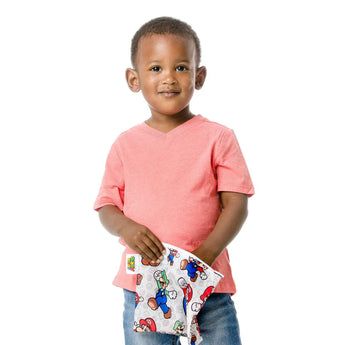 A young boy in a coral shirt and jeans holds a Bumkins Reusable Snack Bag, Large: Super Mario™ & Luigi on a white background.