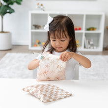 Load image into Gallery viewer, At a white table, a girl opens a Bumkins Reusable Snack Bag, Large 2 Pack: Palm Check with shelves in the background; another bag nearby.