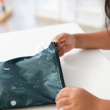 Load image into Gallery viewer, A child zips a Bumkins Reusable Snack Bag, Large 2 Pack: Desert Night at a white table.