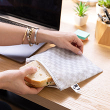 Load image into Gallery viewer, Hands grab a sandwich from a white Roamio by Bumkins Reusable Snack Bag, Large 2 Pack: Rich & Boujee on a desk next to a laptop.