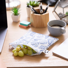 Load image into Gallery viewer, A Roamio by Bumkins Reusable Snack Bag, Large 2 Pack: Coastal holds green grapes on a desk near a coffee cup, notebook, & office supplies.