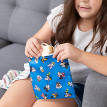 Load image into Gallery viewer, A girl removes a sandwich from Bumkins Reusable Snack Bag, Large 2 Pack: Mickey & Friends MVP while on the couch.