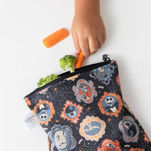 Load image into Gallery viewer, A child reaches for carrots and broccoli from a Bumkins Reusable Snack Bag, Large 2 Pack: Everyday Is Halloween on a white table.