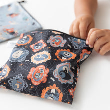 Load image into Gallery viewer, A child opens a Bumkins Reusable Snack Bag, Large 2 Pack: Everyday Is Halloween at a white table.
