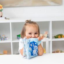 Load image into Gallery viewer, A smiling child holds Bumkins Reusable Snack Bag, Large 2 Pack: Stitch Star-ring Up Trouble at a table in front of toys on white shelves.