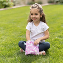 Load image into Gallery viewer, A girl with long hair sits on grass, smiling while holding a Bumkins Reusable Snack Bag, Large 2-Pack: Rainbows & Unicorns.
