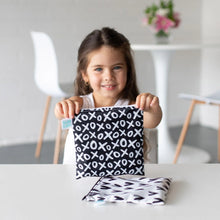 Load image into Gallery viewer, A girl smiles while holding a Bumkins Reusable Snack Bag, Large 2-Pack: XOXO & Hearts as another sits beside her at a white table.